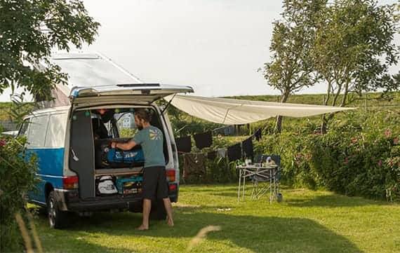 Campervan with a sun sail on a pitch by the embankment