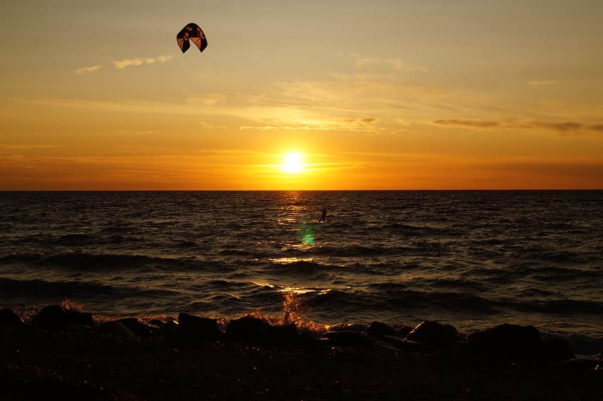 Kitesurfer tegen de ondergaande zon boven de Oostzee