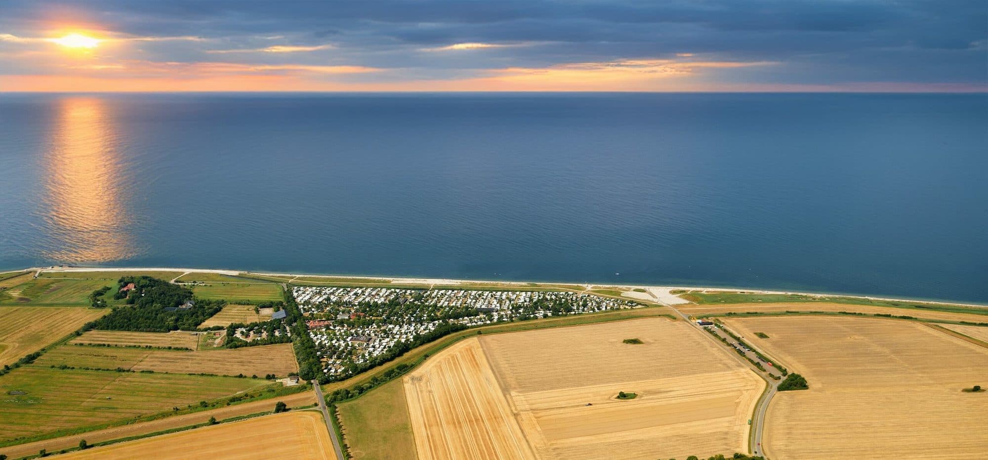 Luftaufnahme des Strandcamping Wallnau zwischen Kornfeldern und der Ostsee, kurz vor Sonnenuntergang